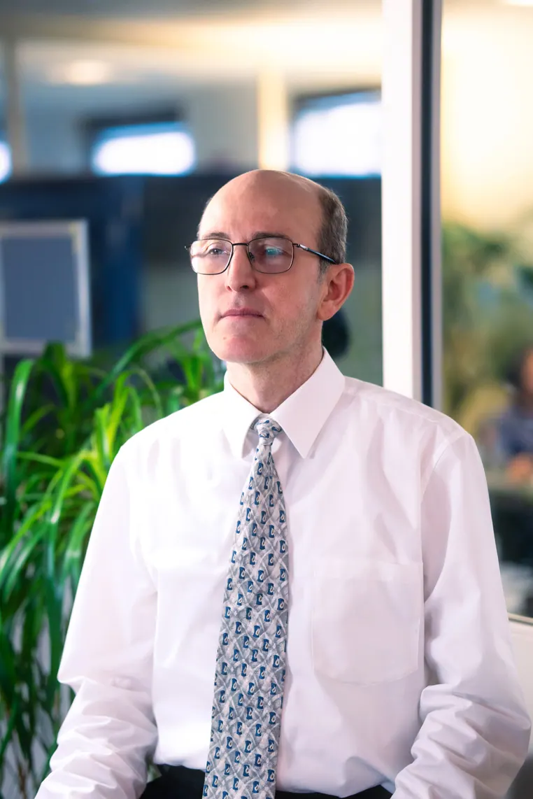 Portrait corporate assis près d'une baie vitrée, en lumière naturelle : collaborateur en chemise blanche et cravate