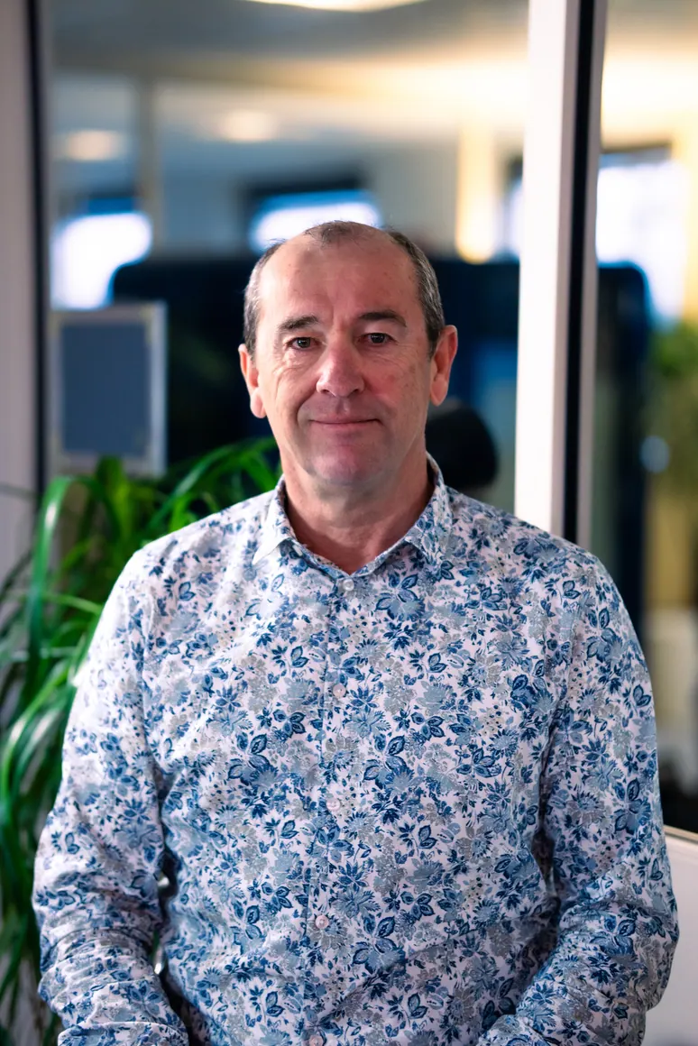Portrait corporate assis près d'une baie vitrée, en lumière naturelle : collaborateur en chemise fleurie