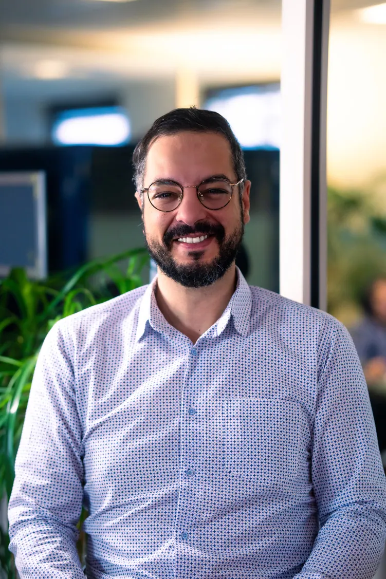 Portrait corporate assis près d'une baie vitrée, en lumière naturelle : collaborateur en chemise claire