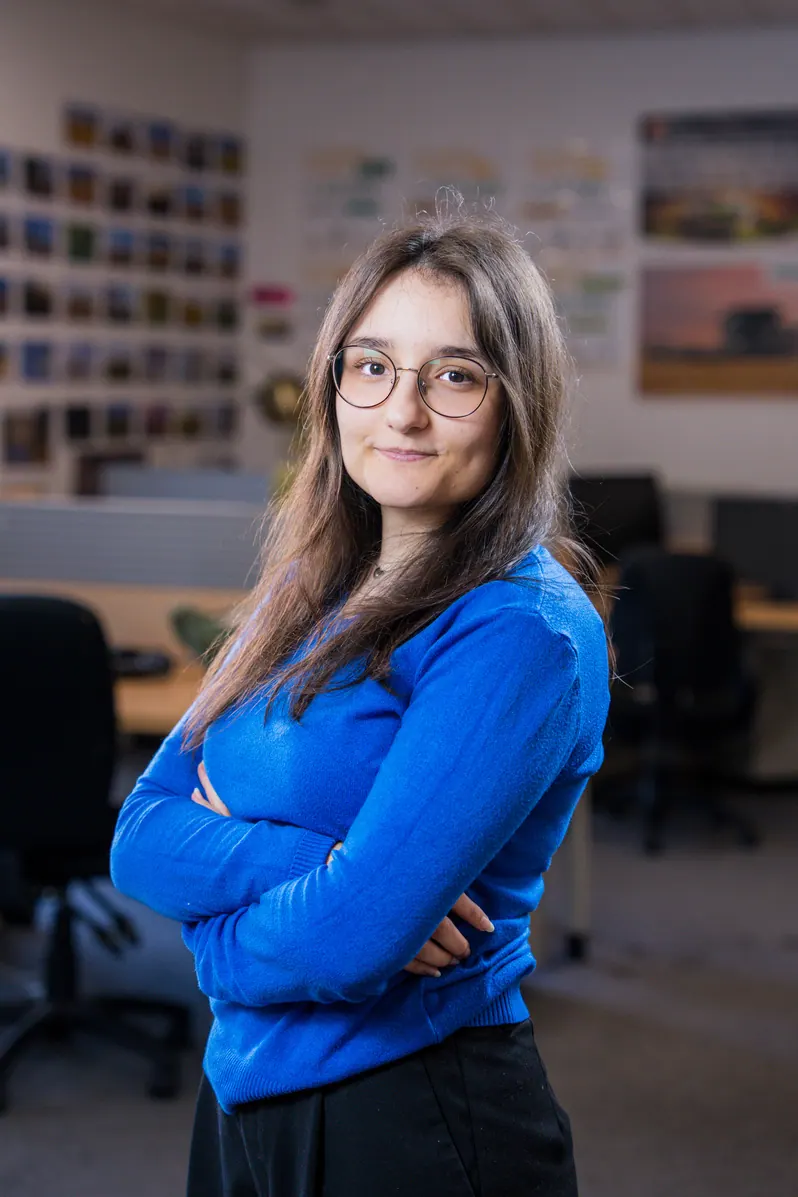 Portrait corporate debout au bureau, bras croisés : collaboratrice en pull bleu