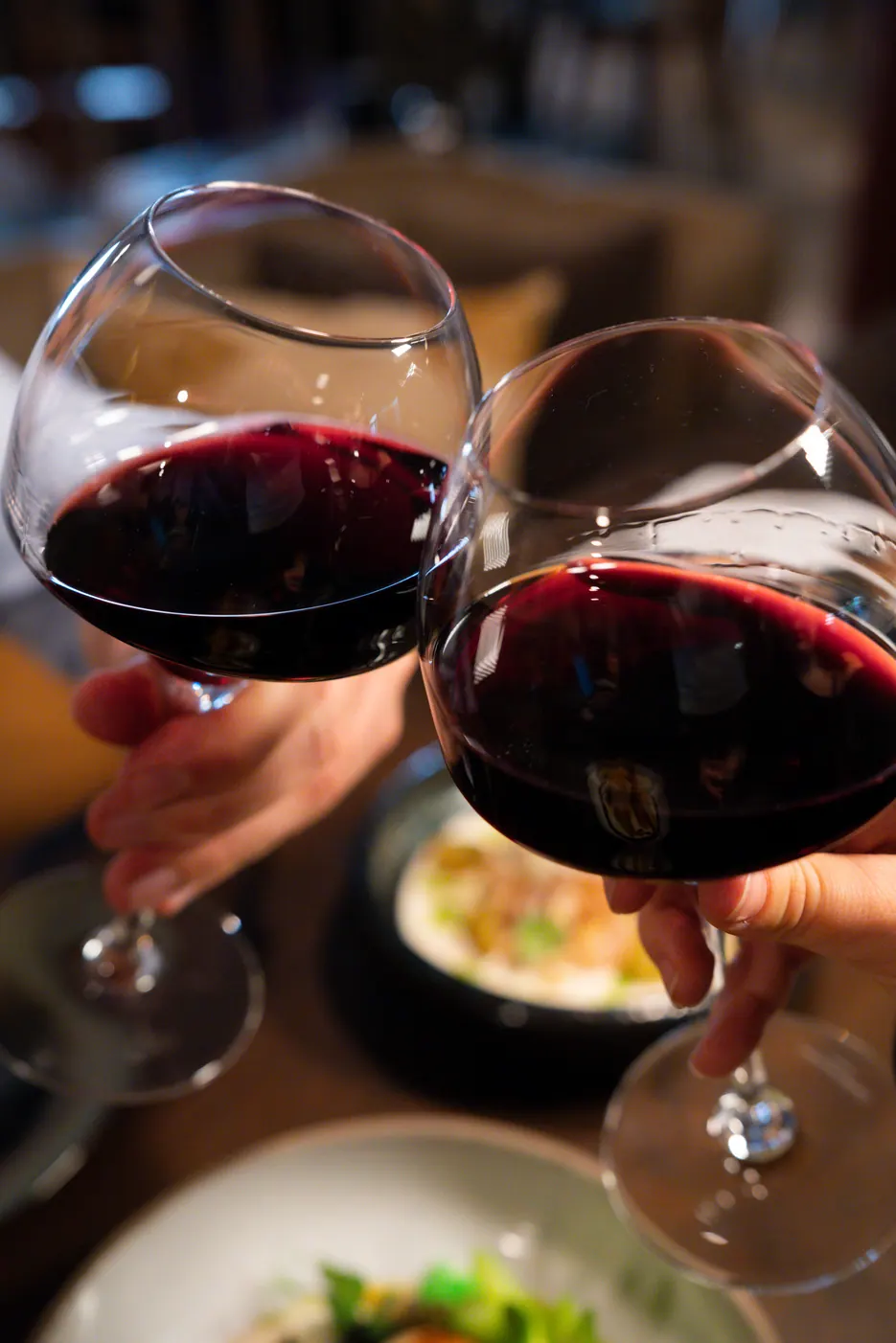 Deux verres de vin rouge qui trinquent au-dessus des assiettes