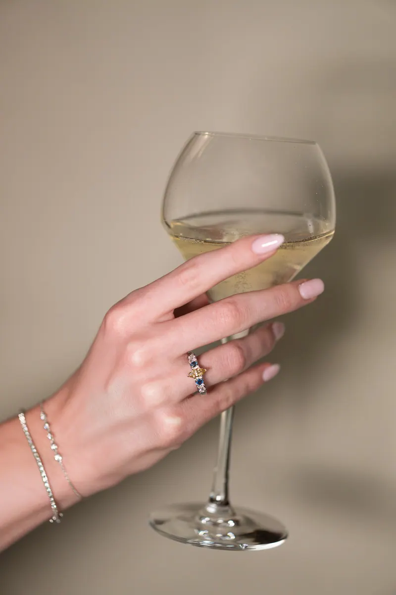 Main tenant un verre de vin, bracelet et bague