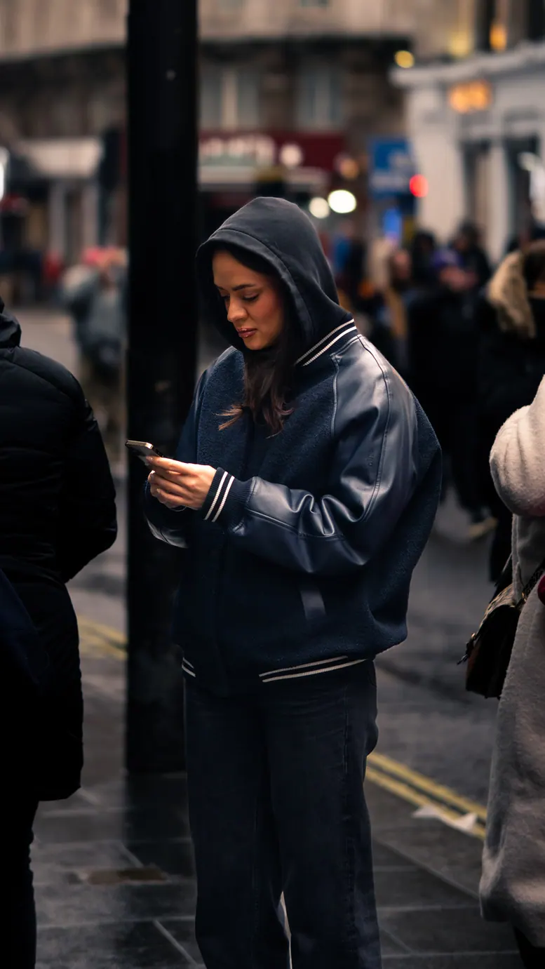 Femme en sweat à capuche sur son téléphone, dans la foule